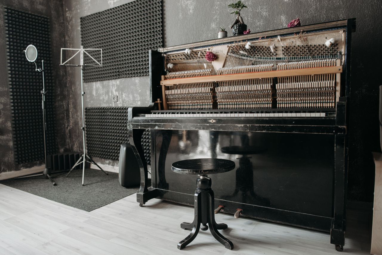 An open vintage upright piano in a soundproof music studio with recording equipment.